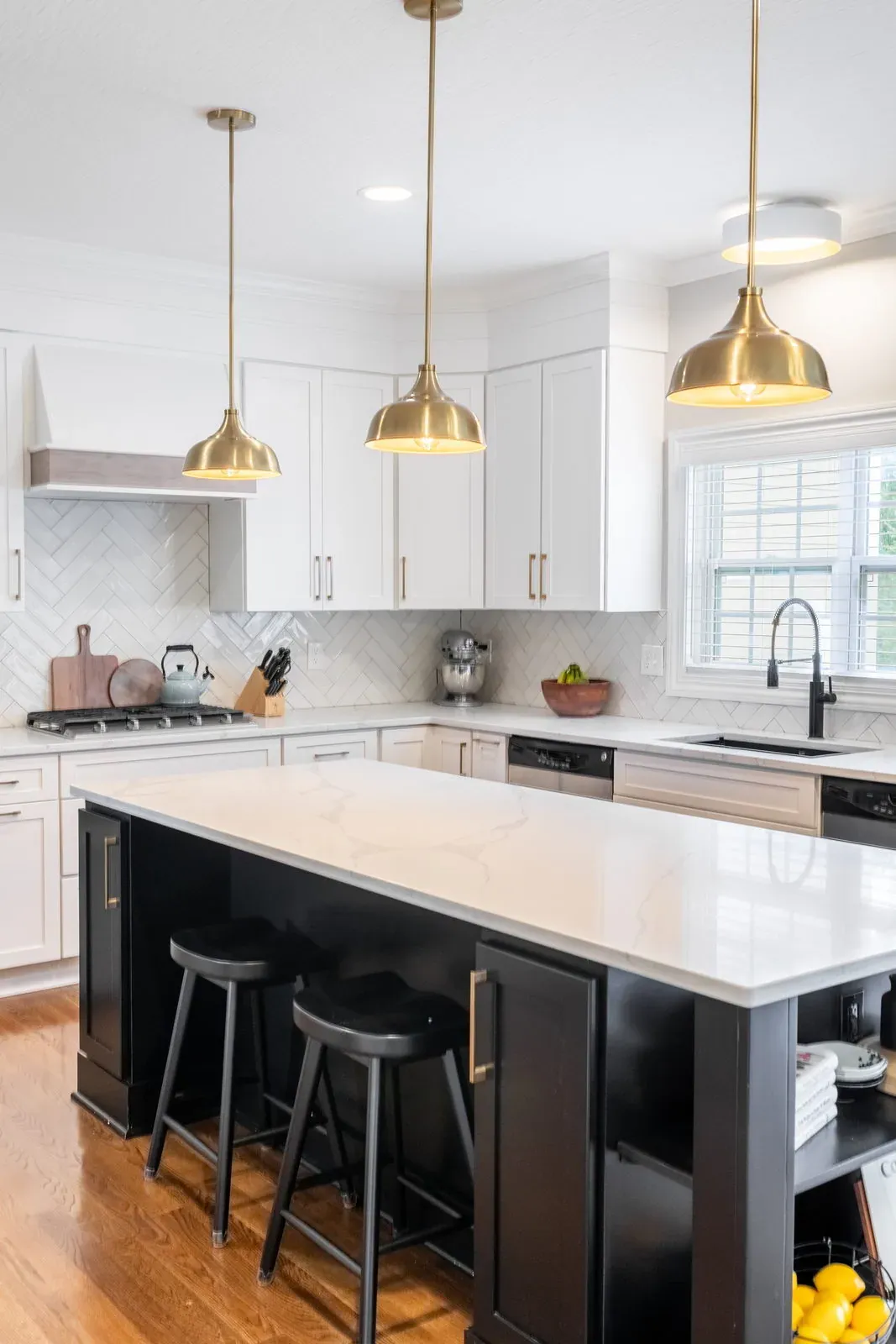 White shaker kitchen with a black island, quartz countertops, counter stools and brass dome pendants over the seating