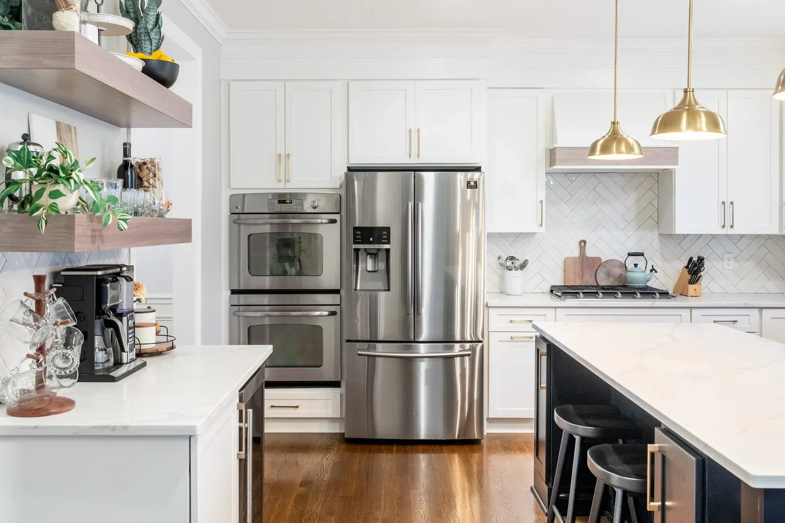 Refaced kitchen with white shaker cabinets, stainless double wall ovens, a black island with quartz top and warm hardwood floors