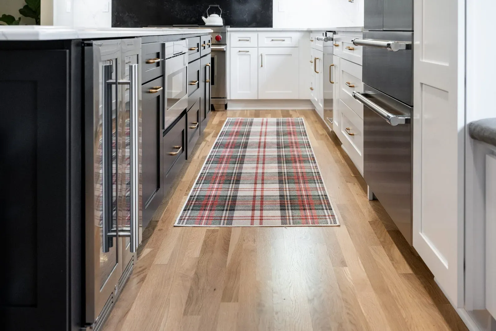 Galley run of custom cabinetry in black and white with integrated appliances, brass pulls and white oak plank flooring