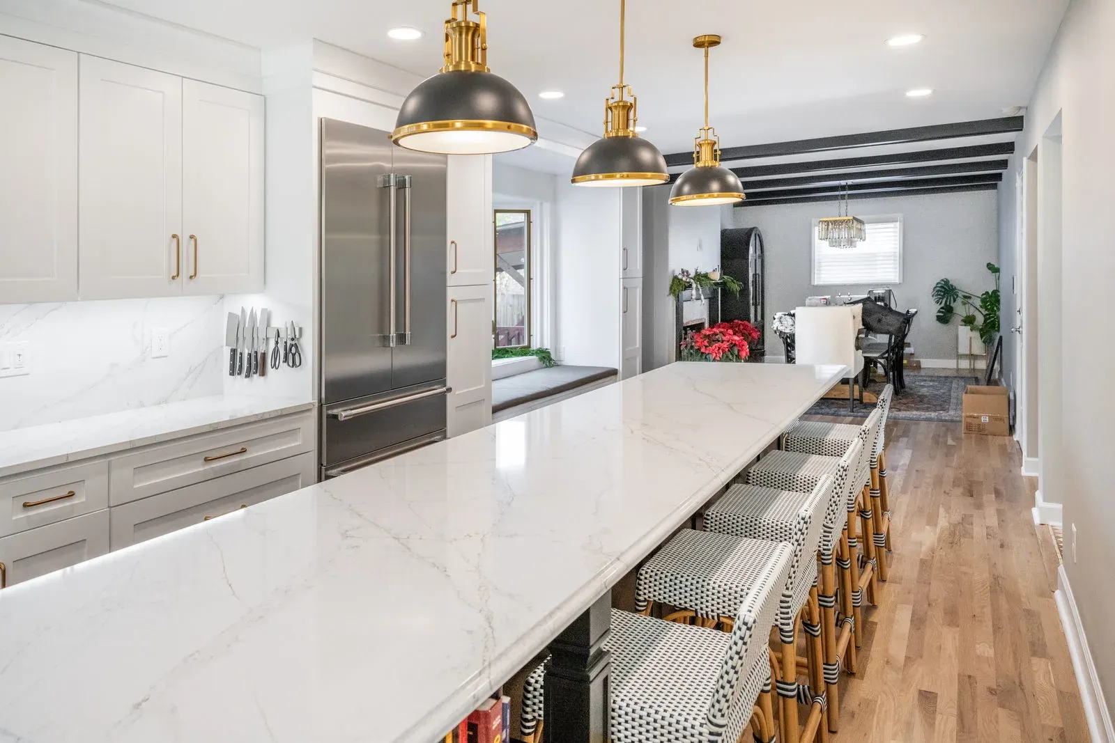 Long custom island with a thick quartz top, rattan counter stools, black dome pendants and a panel-ready built-in refrigerator