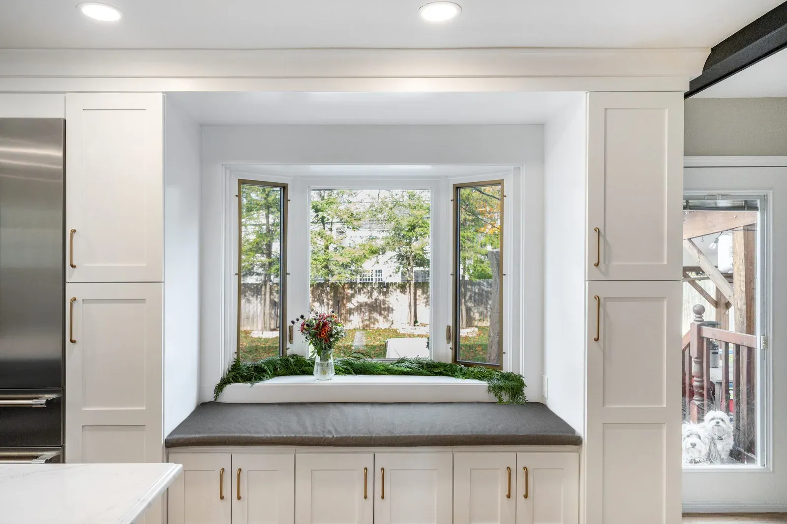Custom cabinetry built around a bay window seat with drawer storage below and full-height painted pantry cabinets on either side