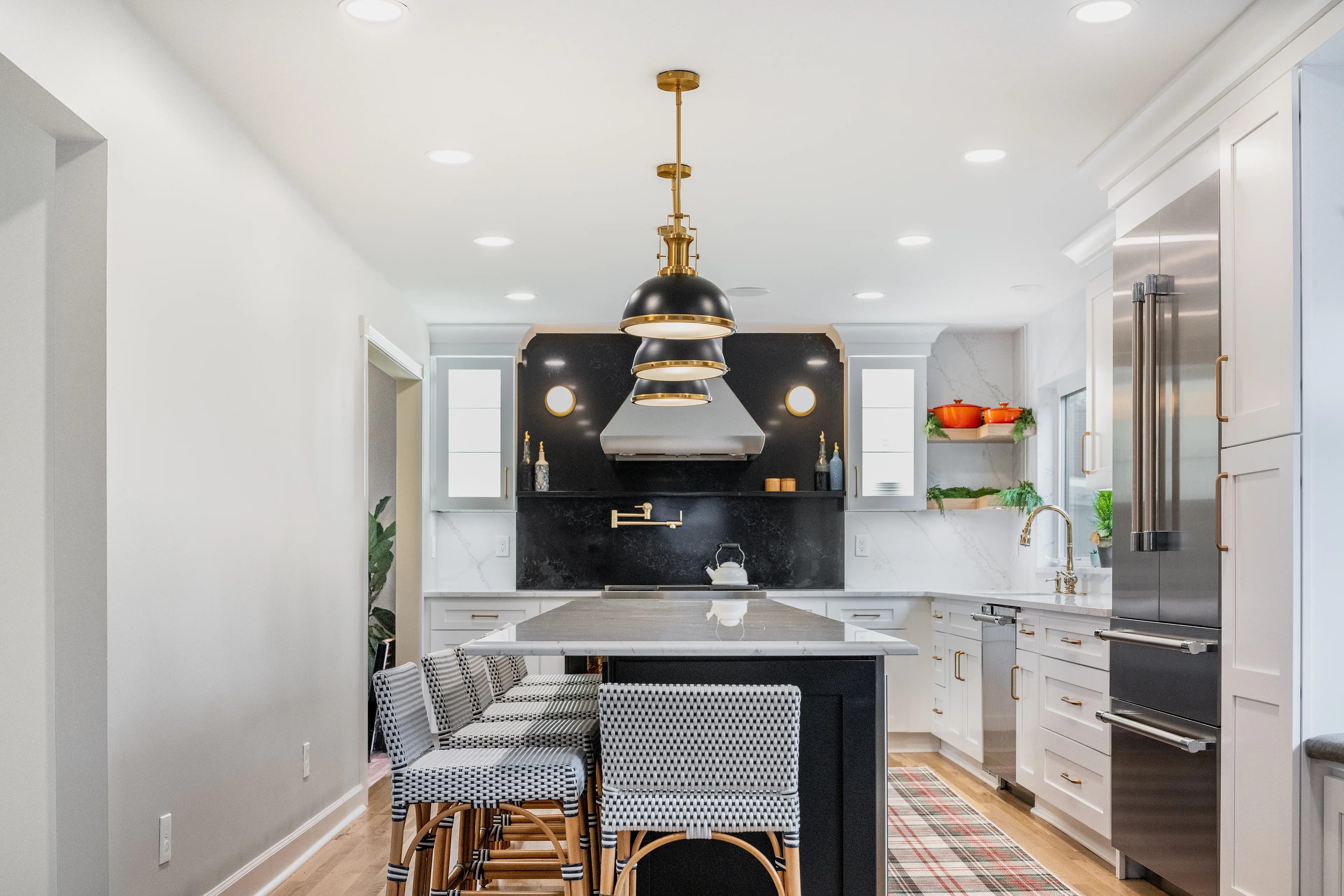 Custom kitchen cabinets in Columbus with a soapstone-look range wall, stainless canopy hood, white inset cabinetry and a black island with quartz top