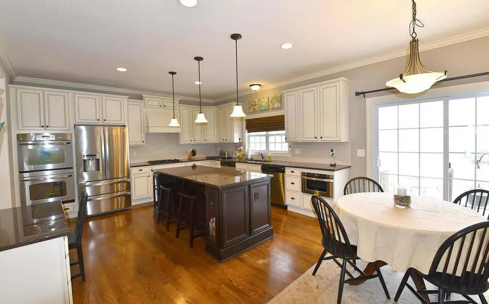 Kitchen before refacing, with cream raised-panel cabinets, a cherry-stained island and granite countertops seen from the dining area