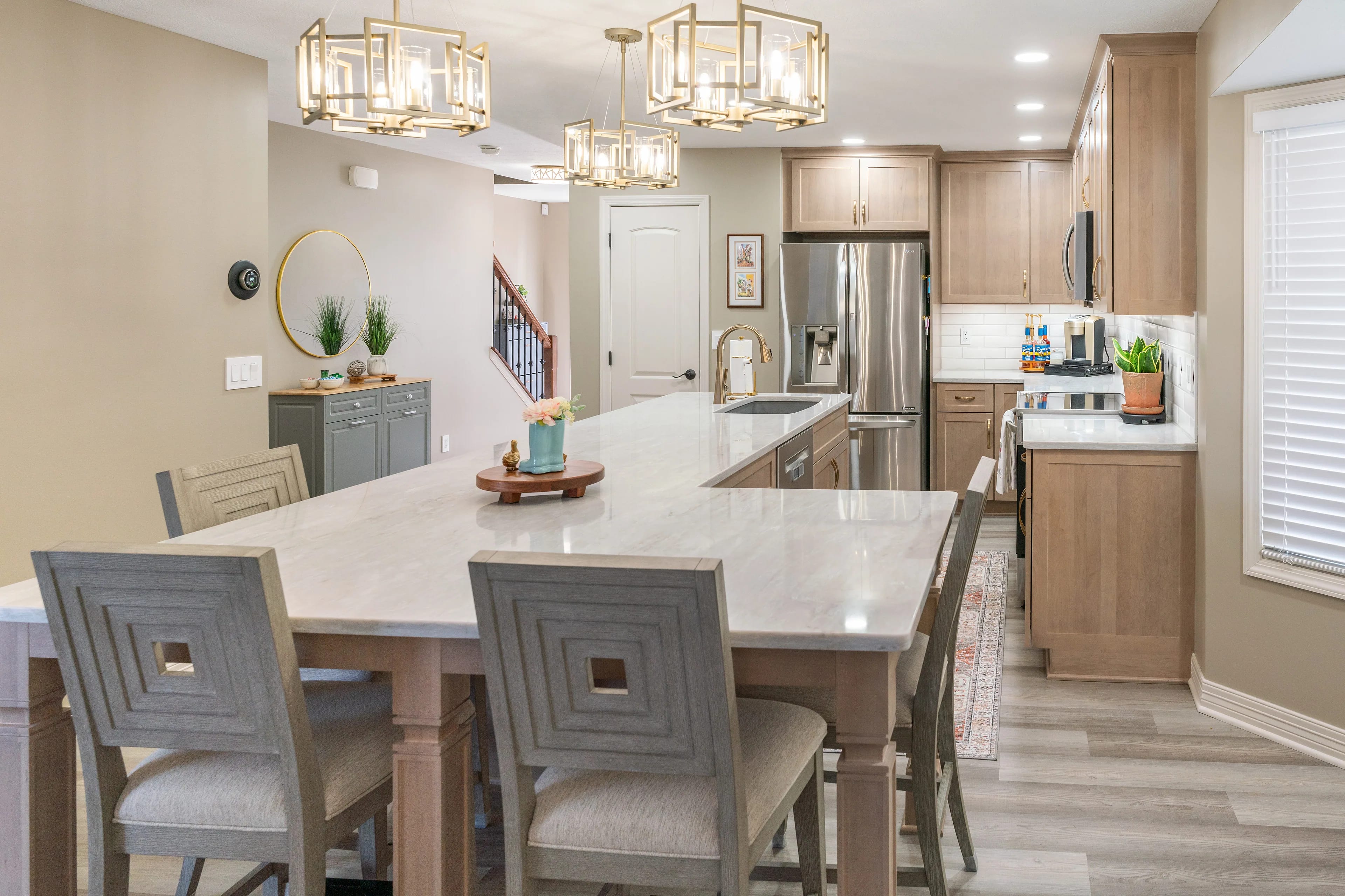 Refaced natural maple kitchen with a long quartz island seating six, brass lantern pendants and a stainless refrigerator on the far run