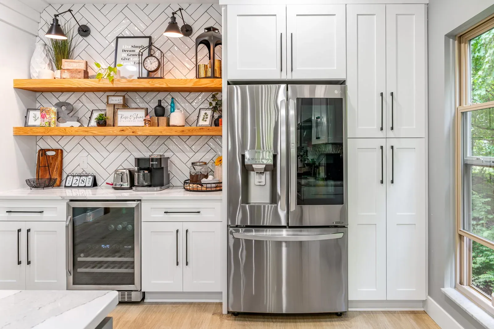 Kitchen beverage center with stained wood floating shelves, herringbone tile, an undercounter wine fridge and a counter-depth stainless refrigerator