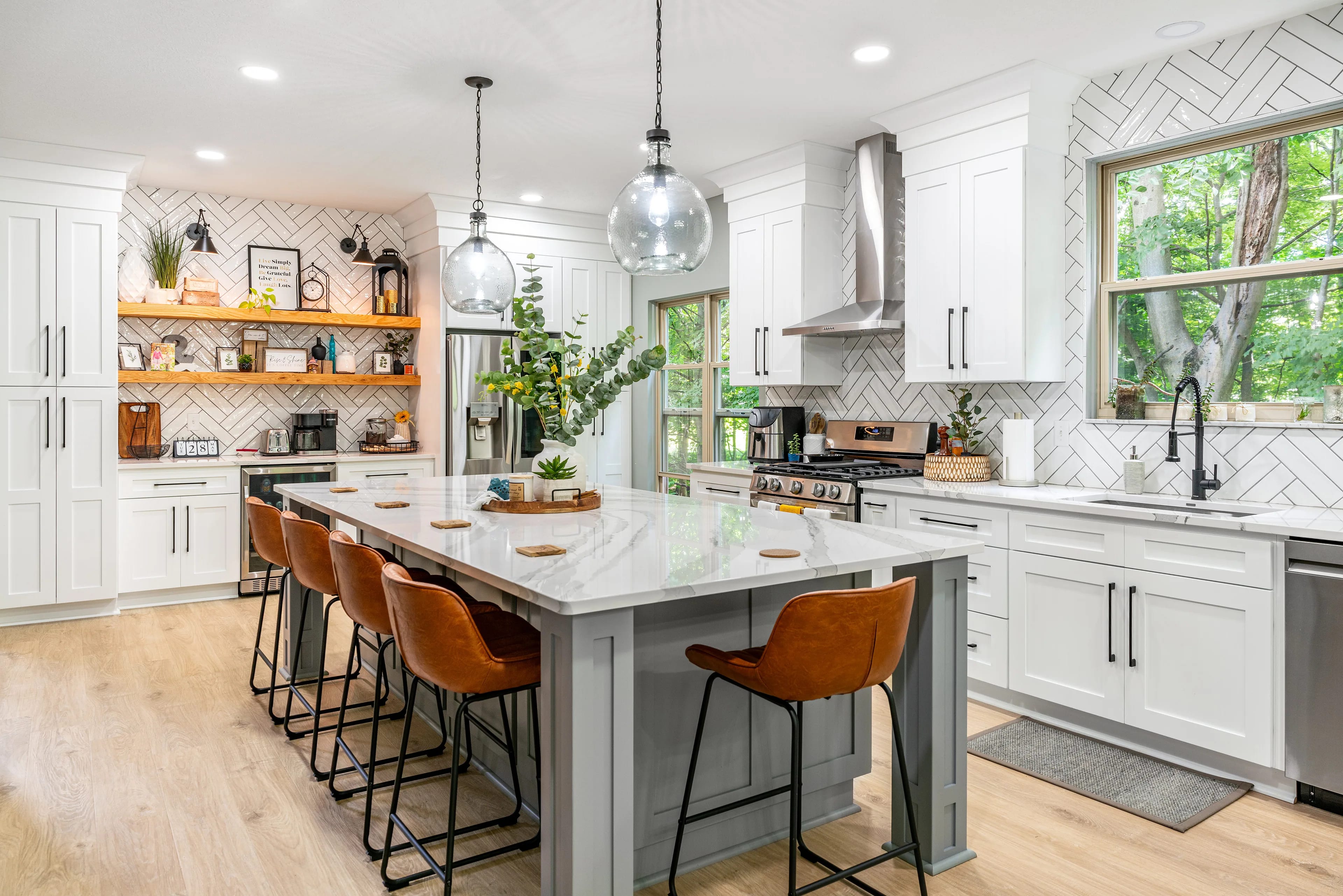 Open-concept kitchen remodel with a quartz-topped grey island, leather counter stools, white shaker cabinets and a white herringbone tile backsplash