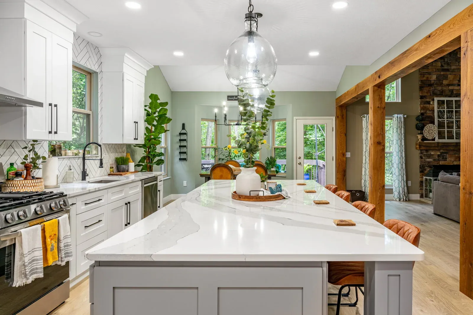 Open-concept kitchen remodel with a large quartz waterfall-edge island, white shaker perimeter cabinets and a timber-framed opening to the great room