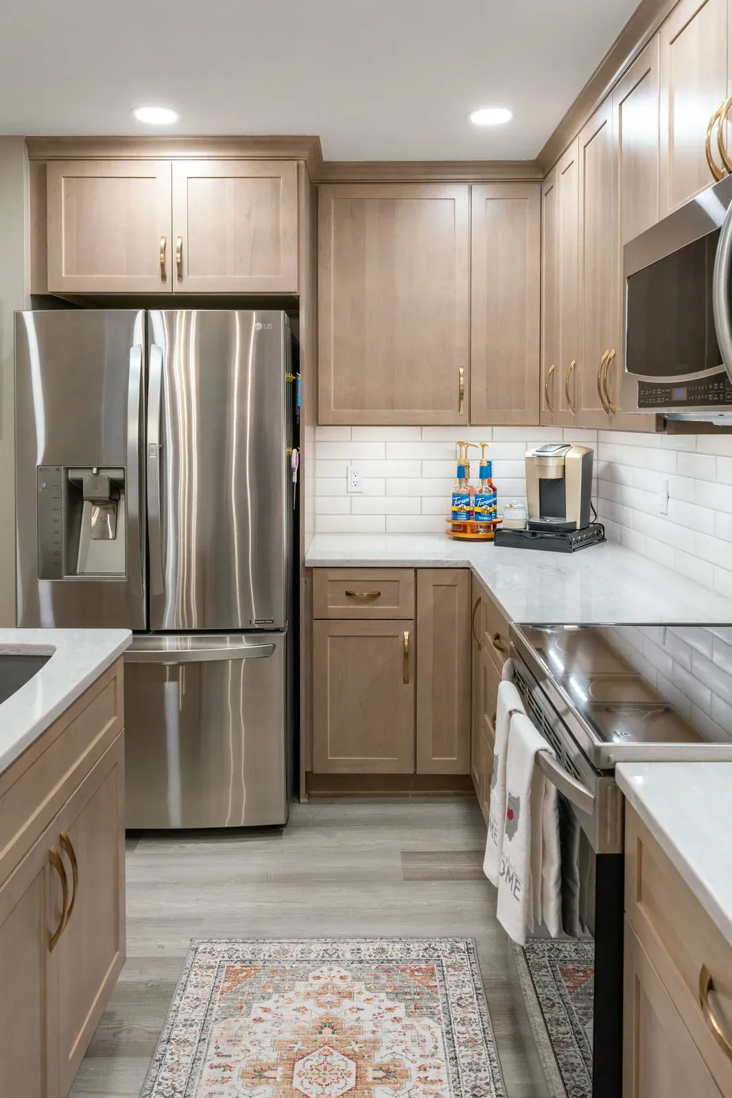 The same refrigerator and range wall after refacing, with light natural maple shaker doors, brass bar pulls, white subway tile and quartz countertops