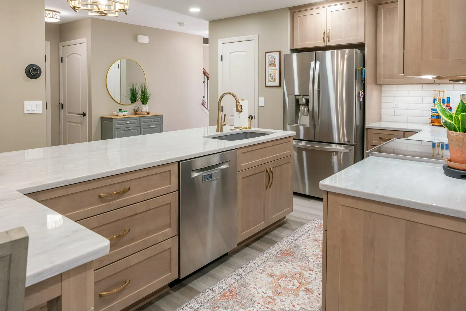 The same L-shaped run after refacing, with natural maple shaker fronts, a single-bowl undermount sink, quartz countertops and a brass faucet