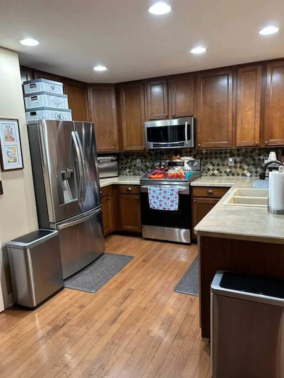 Kitchen before refacing, with dark cherry cabinets, a mosaic tile backsplash and beige laminate countertops around the refrigerator and range wall