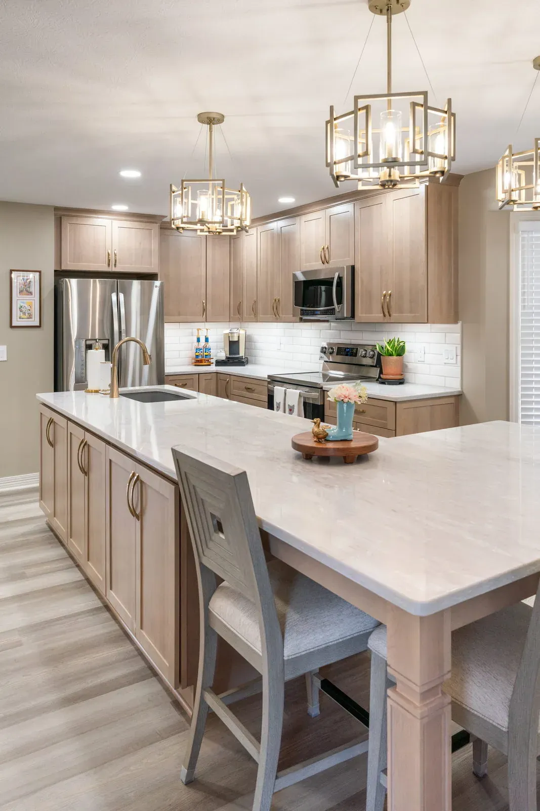Light wood kitchen island with an attached quartz dining table, upholstered chairs and lantern pendants overhead