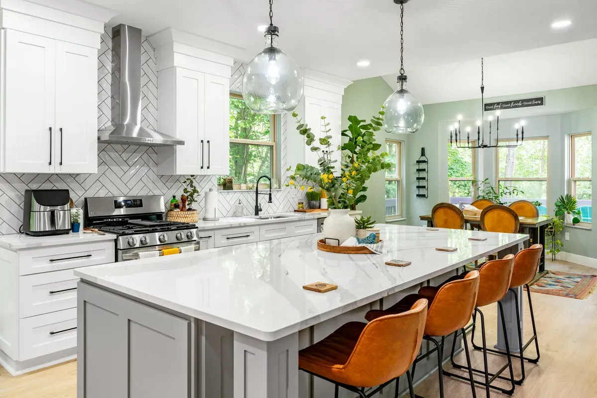 Remodeled open-concept kitchen with a quartz island, leather counter stools, white shaker cabinets and a herringbone tile backsplash
