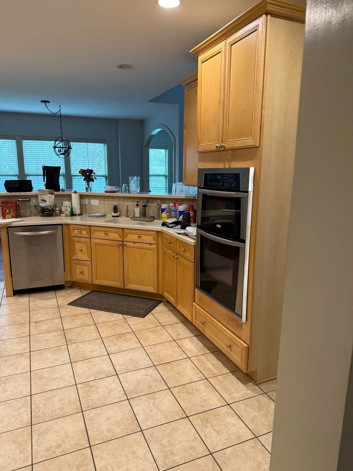 Westerville kitchen before remodeling, with a maple corner sink cabinet, laminate counters, black double wall ovens and ceramic tile flooring