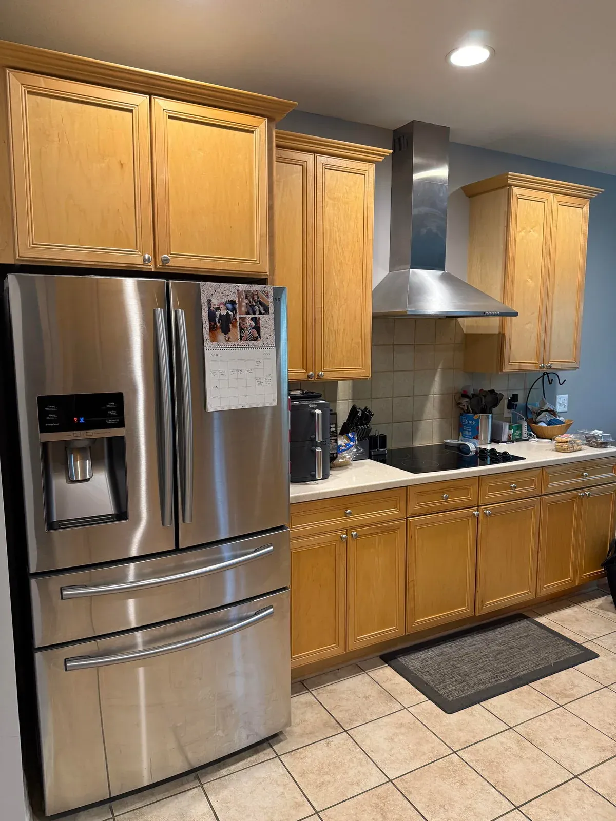 Westerville kitchen before remodeling, with honey maple cabinets, a stainless wall hood, tile backsplash and beige ceramic tile flooring