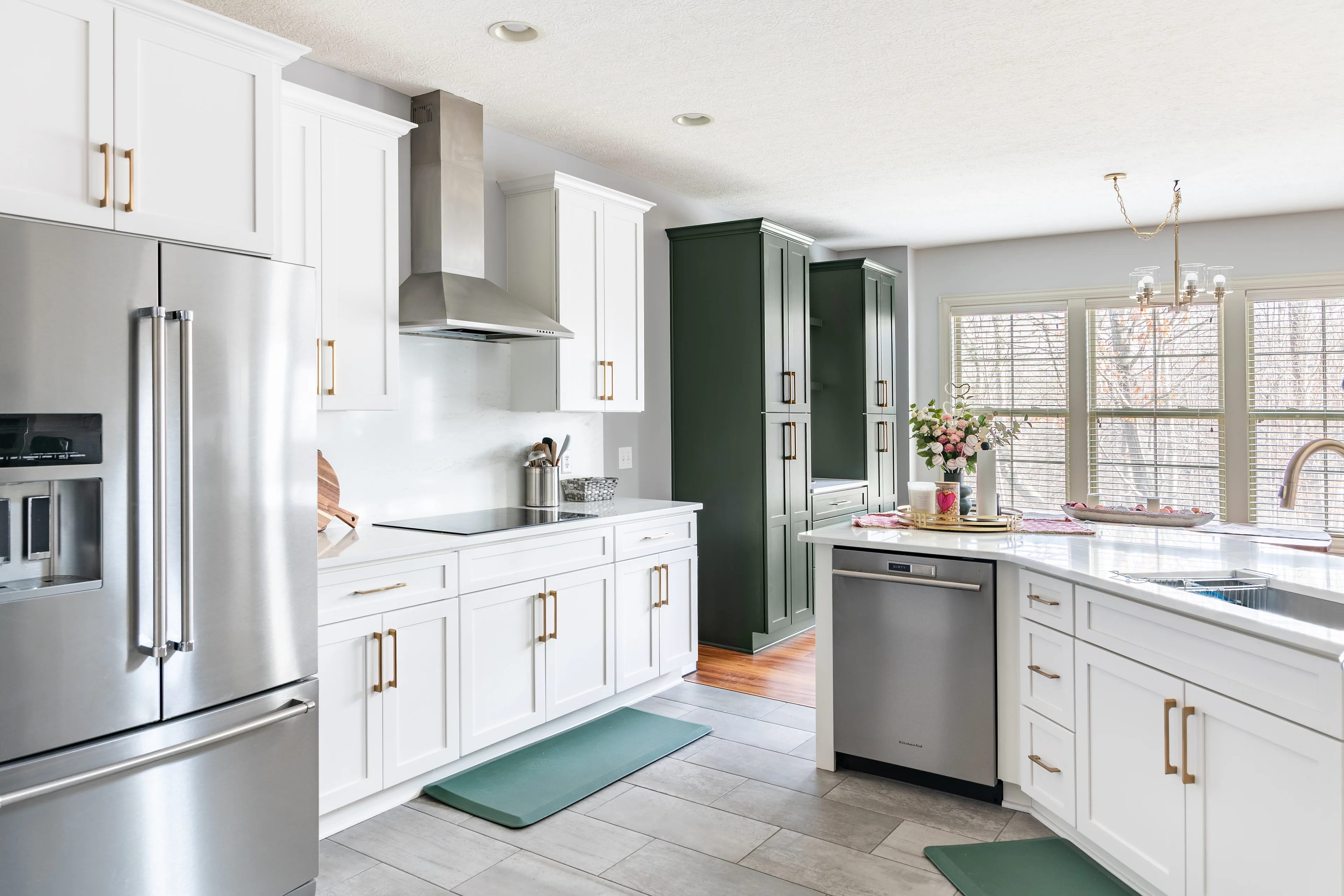 Westerville kitchen remodel with white shaker cabinets, a stainless chimney hood over the range, floor-to-ceiling hunter green pantry cabinets and a window wall above the sink run