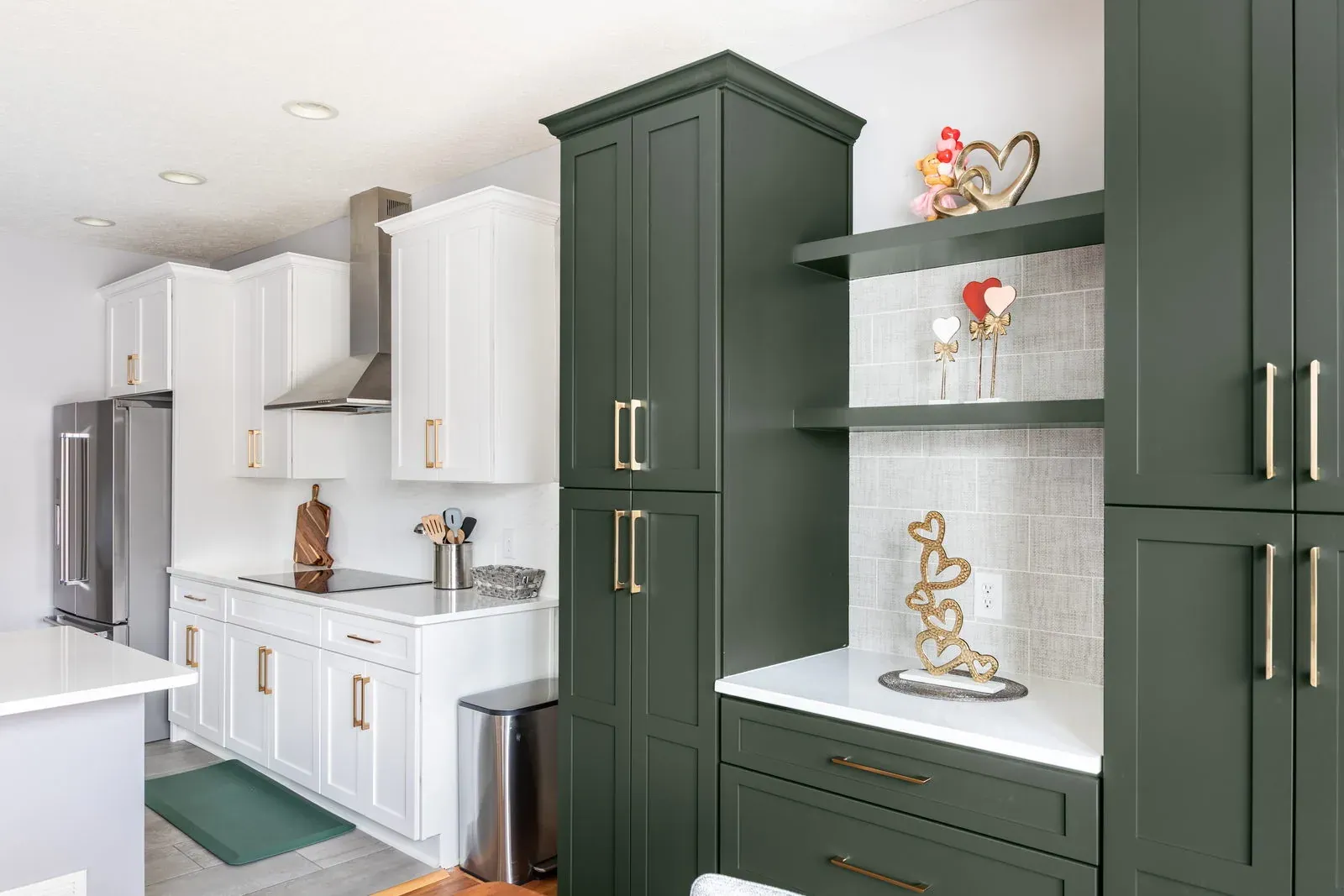 Two-tone kitchen with white perimeter cabinets, a stainless chimney hood and floor-to-ceiling hunter green cabinets with open display shelving